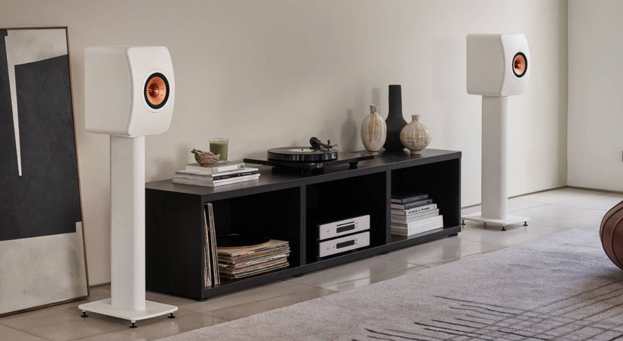 Modernes Wohnzimmer mit weißen KEF‑Regallautsprechern auf Ständern, Vinylschallplatten und einem Plattenspieler auf einem niedrigen Medienmöbel.