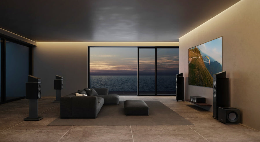 Luxuriöses, modernes Wohnzimmer mit KEF-Standlautsprechern, wandmontiertem Fernseher und Blick auf den Ozean durch raumhohe Fenster, gestaltet für ein beeindruckendes Heimkinoerlebnis.