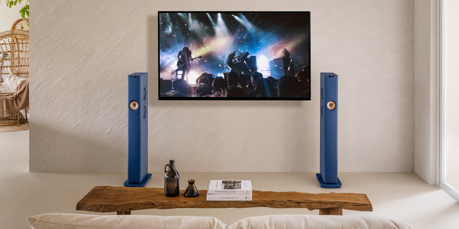 KEF LS60 Wireless-System mit TV-Gerät, auf dem ein Live-Konzert in einem Wohnzimmer läuft