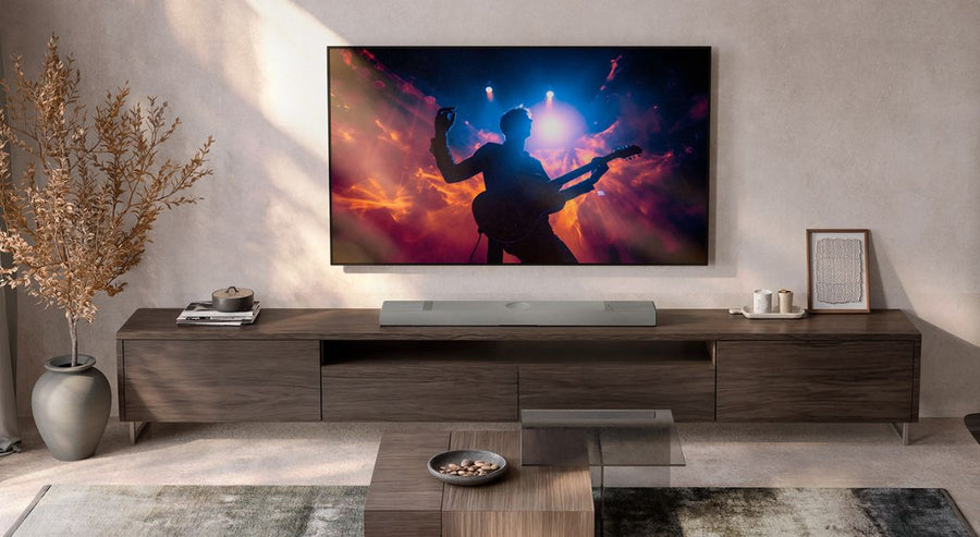 Wandmontierter Fernseher, der die Silhouette eines Gitarristen bei einem Livekonzert zeigt, über einem modernen Medienmöbel aus Holz mit schlanker Soundbar.